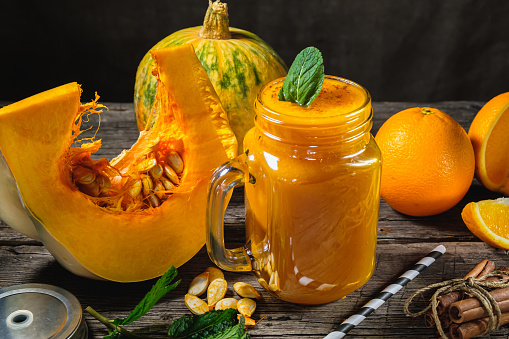 Pumpkin smoothies with mint leaves with a piece or pieces of raw pumpkin and orange in jar with mint leaf on wooden background. horizontal orientetion.