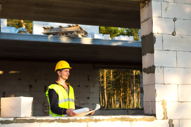 istock A construction engineer and designer in a yellow hardhat studies a drawing of a building on a construction site. A house made of porous concrete blocks, a worker in the process at the window and wall 1334300936