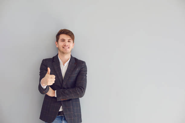 istock Smiling man thumb up in a casual jacket on a gray background. 1334305673