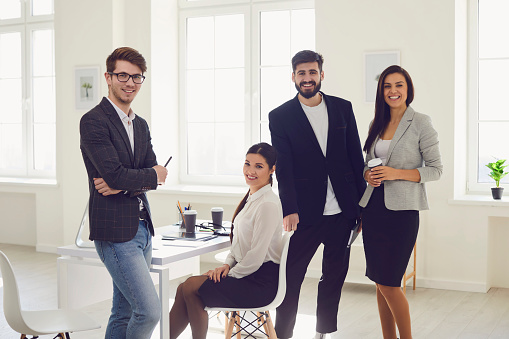 Group of business people standing looking smiling standing at a table in the office. Group of serious businesswomen businessmen discuss collaborate analyze reports work finances brainstorm team work at briefing meeting.