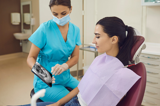 Young woman doctor dentist in medical mask showing panoramic x-ray snapshot of teeth to young patient woman in dental clinic. Dental care and visiting dentist concept