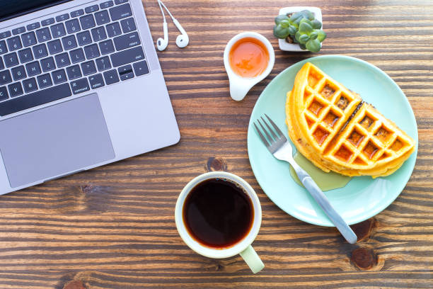 istock Top table view flat lay on a desk with a laptop computer, cup of coffee and Waffle on green plate with honey cup and cell phone earbuds. Concept of morning working with easy breakfast, ready to work. 1334308263
