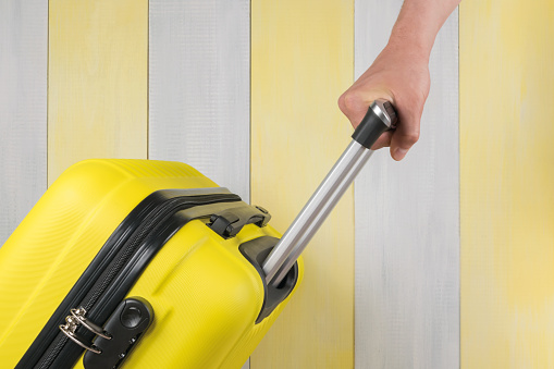 hand carries a suitcase on a gray-yellow background, close-up, side view