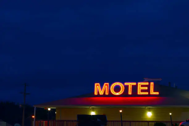 A neon sign reading MOTEL,  glows at dusk with a clear, blue sky in the background.