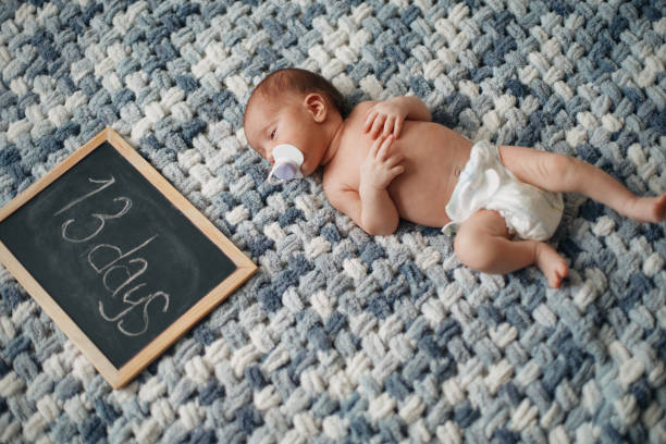 書き込みボードの隣に横たわっているおしゃぶりを持つ新生児 - baby holding babies only sign ストックフォトと画像