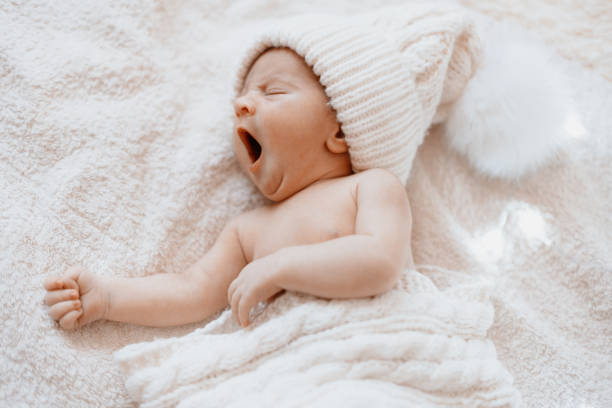 cute yawning newborn baby in a white knitted hat stock photo