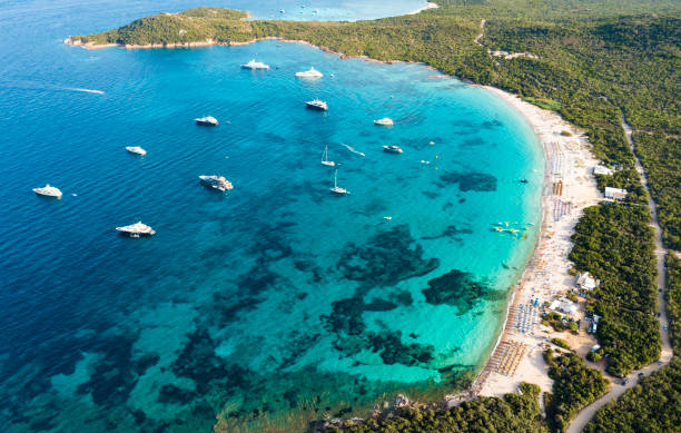 View from above, stunning aerial view of a green coastline with a white sand beach and and boats sailing on a turquoise water at sunset. Cala di volpe beach, Costa Smeralda, Sardinia, Italy. View from above, stunning aerial view of a green coastline with a white sand beach and and boats sailing on a turquoise water at sunset. Cala di volpe beach, Costa Smeralda, Sardinia, Italy. Cala Di Volpe stock pictures, royalty-free photos & images