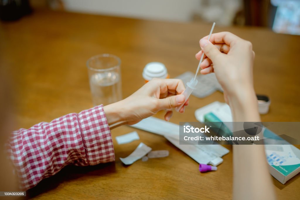Young woman drops swab in a protective plastic tube. Asian woman drops swab in a protective plastic tube after nasal swab test to check for virus at home. Coronavirus Stock Photo