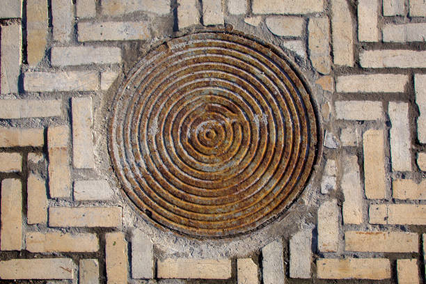 istock iron rusty round manhole on the sidewalk paved with stone tiles top view, old sewer hatch on a brick road. 1334324318