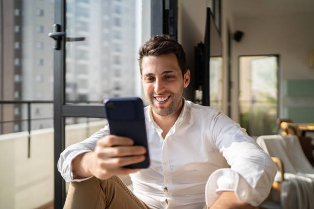 istock Man using smartphone sitting by the window sill at home 1334324631