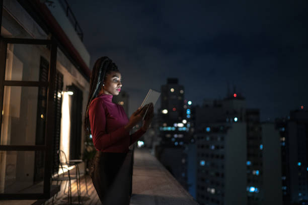 giovane donna che usa il tablet digitale sul balcone dell'appartamento - addiction internet computer working late foto e immagini stock