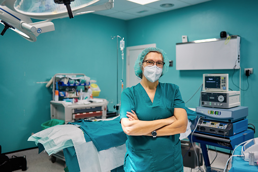 Self assured female doctor in medical uniform looking at camera with folded arms in hospital