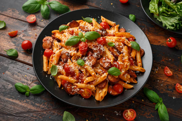 Sausage penne Pasta with tomato sauce, parmesan cheese and basil on black plate Sausage penne Pasta with tomato sauce, parmesan cheese and basil on black plate. marinara stock pictures, royalty-free photos & images