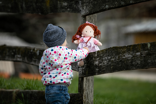 Adorable baby girl playing with a doll outdoors. Little child having fun. Kid playing  with a stuffed toy.