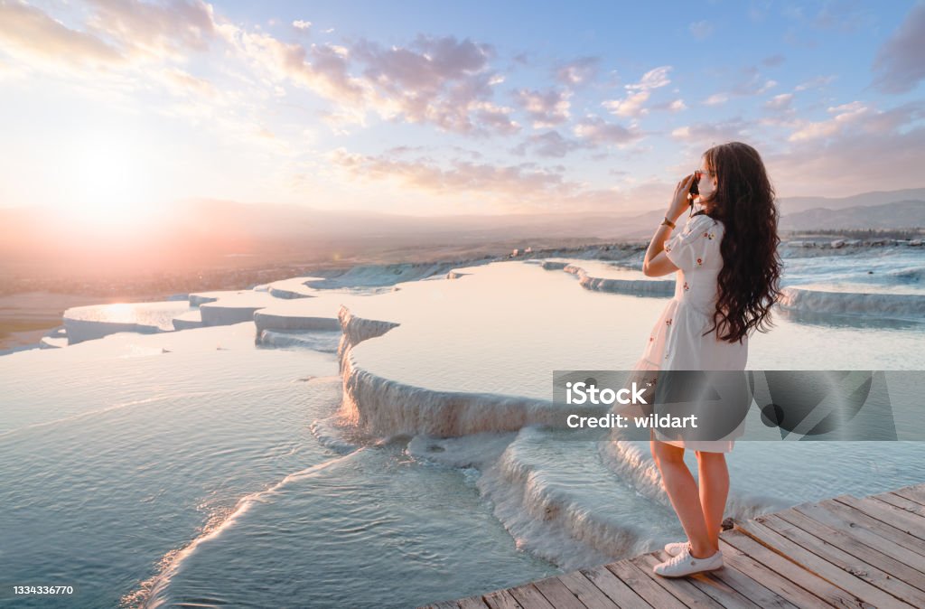 Beautiful traveller photographer girl is taking photos at travertine pools during sunset in Pamukkale UNESCO, Photographer, Camera, Travertine pools, Denizli Pamukkale Stock Photo