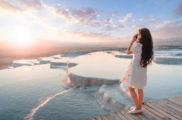 Photo of Beautiful traveller photographer girl is taking photos at travertine pools during sunset in Pamukkale
