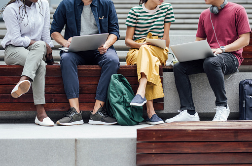 Group of cropped unrecognisable university students sitting outdoors and holding laptops
