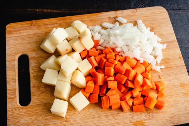 Peeled and diced onion with chopped tomatoes and carrots on a cutting board