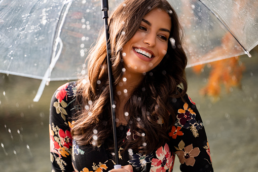 Gorgeous woman smiling and holding umbrella while rain is pouring , closeup shot