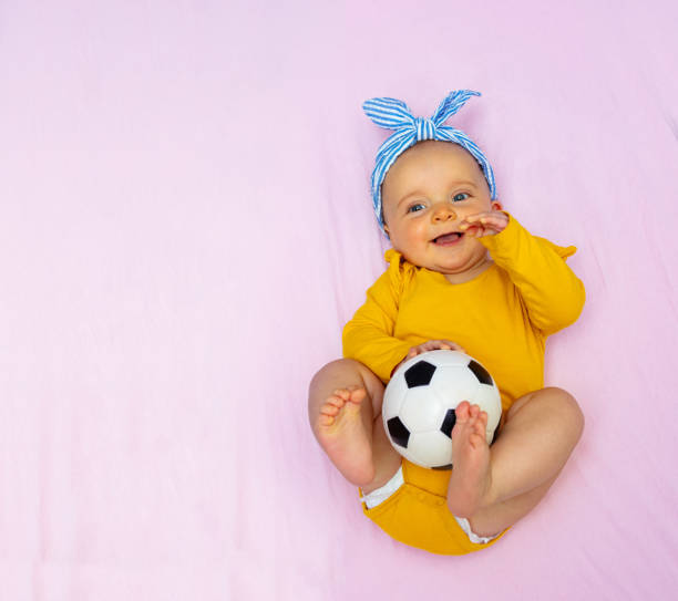 幸せな女の赤ちゃんはサッカーボールのおもちゃでベッドに横たわって - baby people headband portrait ストックフォトと画像