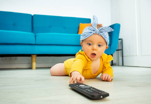 テレビコントロールに達する小さな女の赤ちゃんのストレッチハンド - baby people headband portrait ストックフォトと画像