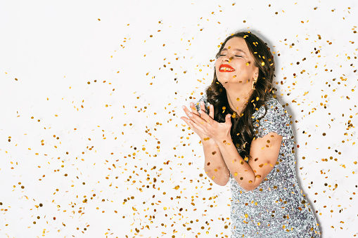 Holiday celebration. Excited woman. Festive decor. Happy beautiful laughing lady enjoying party throwing sparkle golden confetti spangles isolated white copy space.