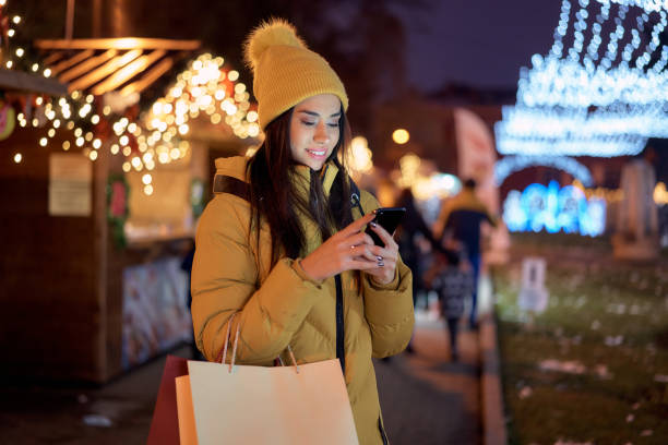 istock Cheerful woman using phone against Christmas lights background 1334361204