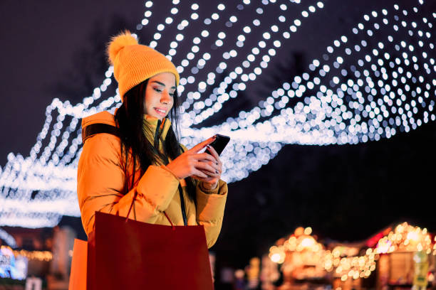 istock Cheerful woman using phone against Christmas lights background 1334361213