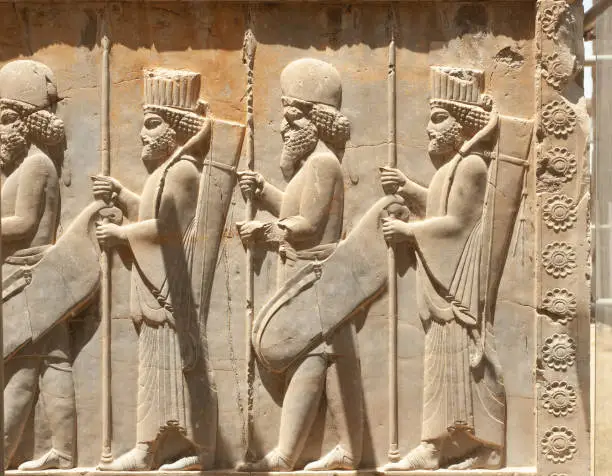 Photo of Soldiers of historical empire with weapon in hands. Stone bas-relief in ancient city Persepolis, Iran. Capital of the Achaemenid Empire (550 - 330 BC). UNESCO declared Persepolis a World Heritage Site