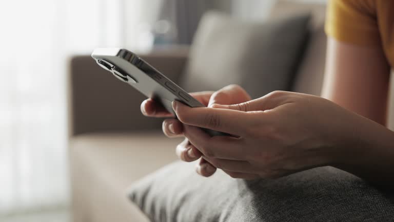 Hand of woman using smartphone in the living room at home, typing message. Close-up of young women hand