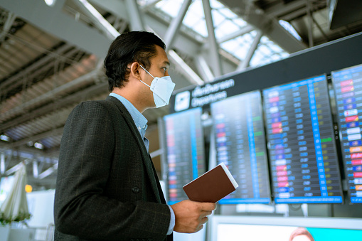 Asian businessman wear mask face protection business travel checking passport information boarding  in terminal airport.