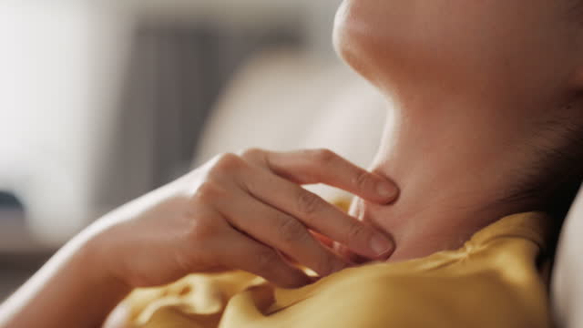 Asian woman hand touching on her neck at home cough and sore throat, close-up