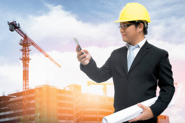 istock Asian designer engineer holding blueprints in his hand and using smartphones to communicate for management. 1334391756