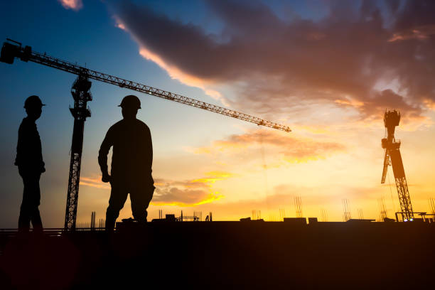 Silhouette engineer construction work control and blurred tower crane background on natural sunset sky.,Heavy industry and building construction work concept. stock photo