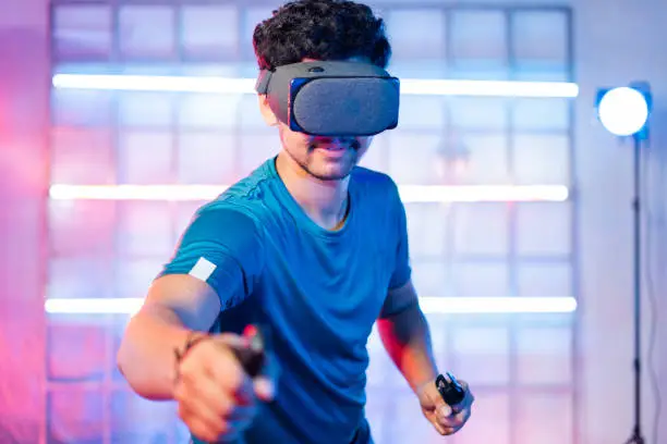 Photo of Young man playing video game by wearing vr or virtual reality goggles and holding joysticks in hands - concept of modern gaming technology