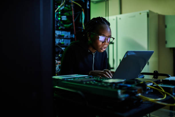 istock Shot of a young female computer programer using a laptop while standing in a dark server room 1334405407