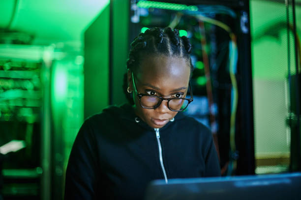 istock Shot of a young female computer programer using a laptop while standing in a dark server room 1334405483