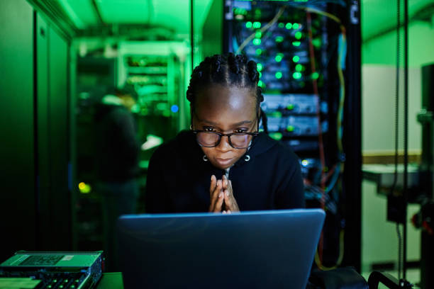 istock Shot of a young female computer programer using a laptop while standing in a dark server room 1334405488