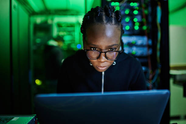 istock Shot of a young female computer programer using a laptop while standing in a dark server room 1334405496