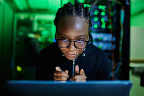 istock Shot of a young female computer programer using a laptop while standing in a dark server room 1334405518