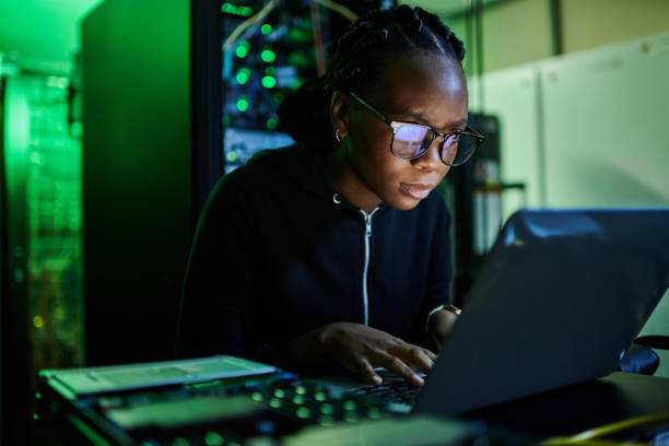 istock Shot of a young female computer programer using a laptop while standing in a dark server room 1334405523