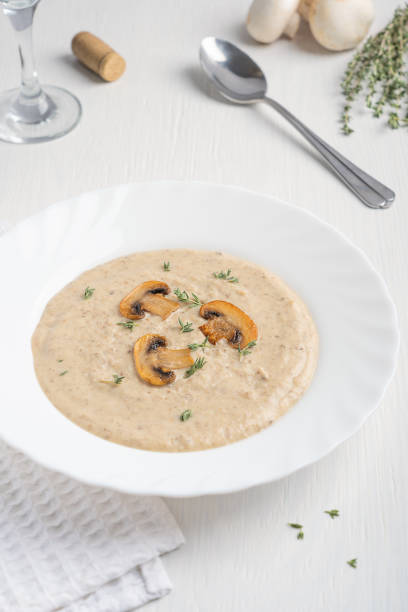 istock Plate with mushroom pureed soup decorated with fried champignon slices and thyme served with glass of wine on white wooden background 1334405820