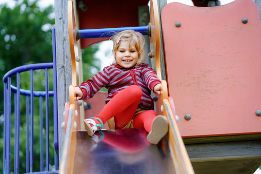 Little preschool girl playing on outdoor playground. Happy toddler child climbing and having fun with summer outdoors activity. Girl slinding down the slide