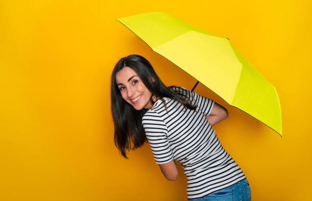 happy smiling young woman hiding under a yellow umbrella and having fun - rain women umbrella parasol imagens e fotografias de stock