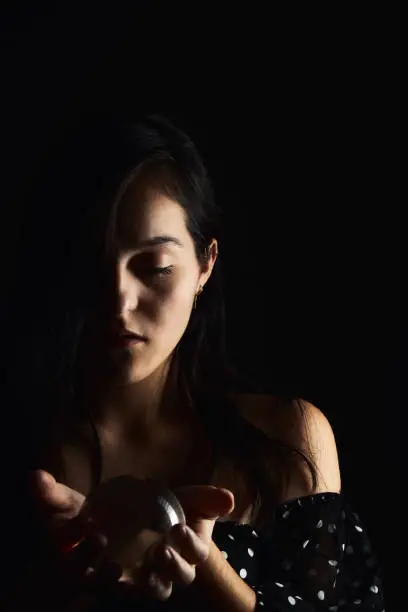 Photo of Hispanic teenager playing with a crystal ball on a black background. Mysticism and fun concept