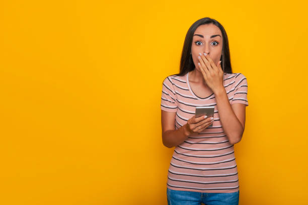 istock Modern beautiful young brunette woman is using smart phone for surfing on the internet and for work isolated on yellow background 1334409225