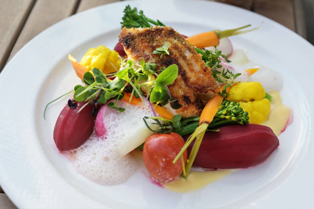 istock Fried fish on vegetables like carrots, cauliflower, beet and tomatoes with saffron sauce and foam, garnished with herbs and sprouts on a white plate 1334421301