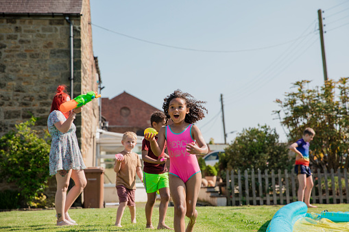 Children playing outside in a garden in the North East of England having a water fight, running around while laughing.
