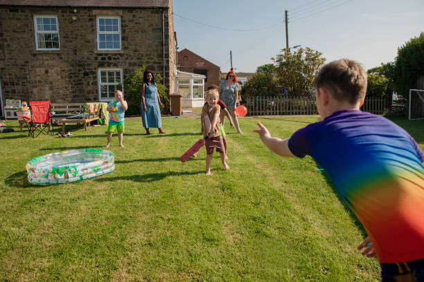 Playing Catch with Water Balloons Children playing outside in a garden in the North East of England having a water fight. They are batting water balloons with a bat. water balloon stock pictures, royalty-free photos & images