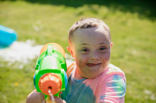 Children playing outside in a garden in the North East of England having a water fight. A boy with down syndrome is looking at the camera while holding a water pistol.